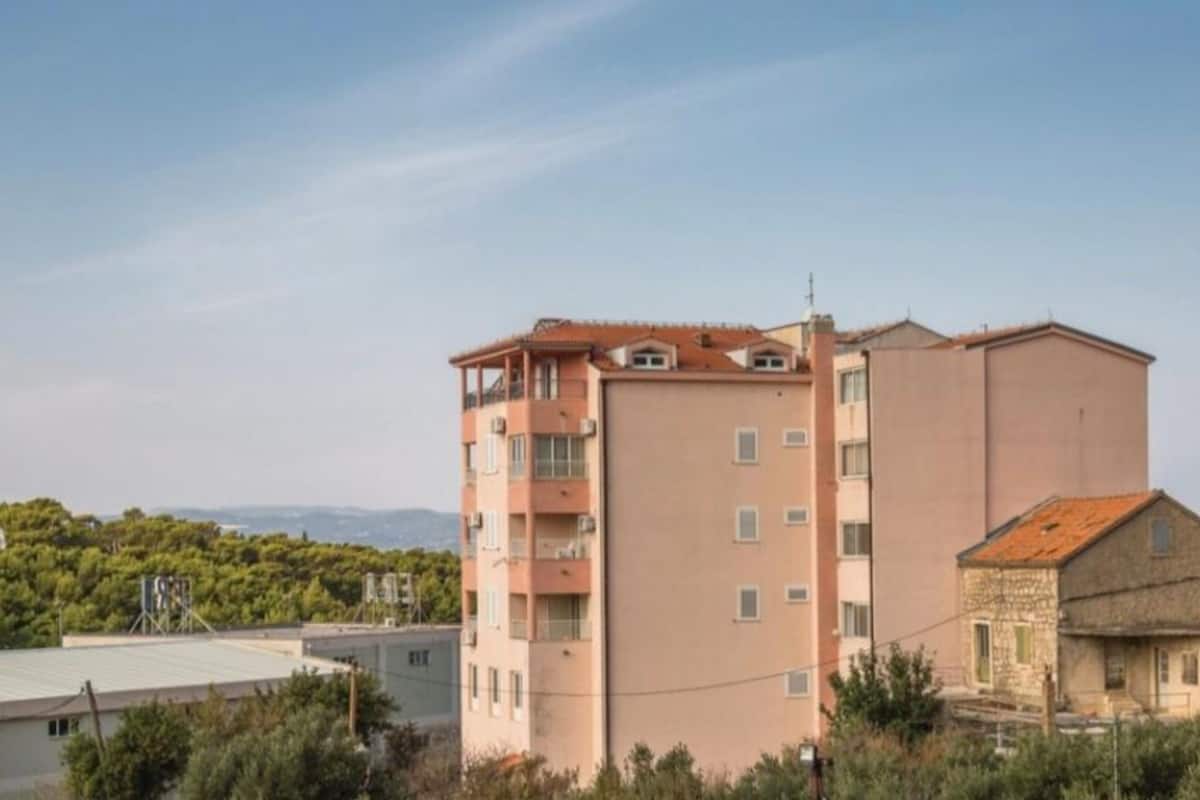 A multi-story building with balconies, a flat roof, and a view of the surrounding landscape.