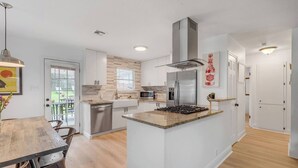 Une cuisine moderne avec des meubles blancs, un îlot central, des appareils en acier inoxydable et une table à manger en bois.