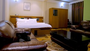 A hotel room with a bed, a wardrobe, a leather sofa, a coffee table, and a television.
