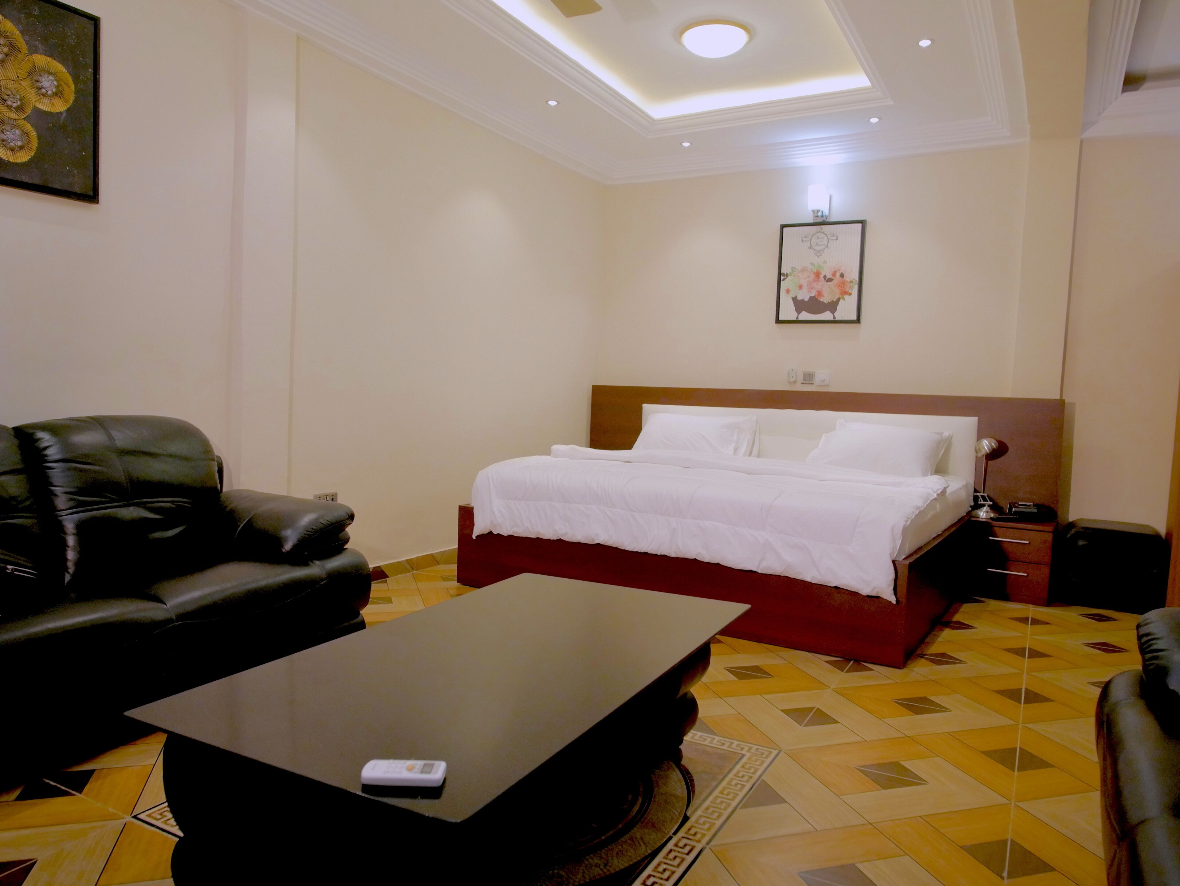 A hotel room with a bed, a black leather sofa, a small table, and a patterned floor.