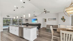 Een moderne keuken met witte kasten, een centraal eiland en een eethoek met een houten tafel en stoelen.