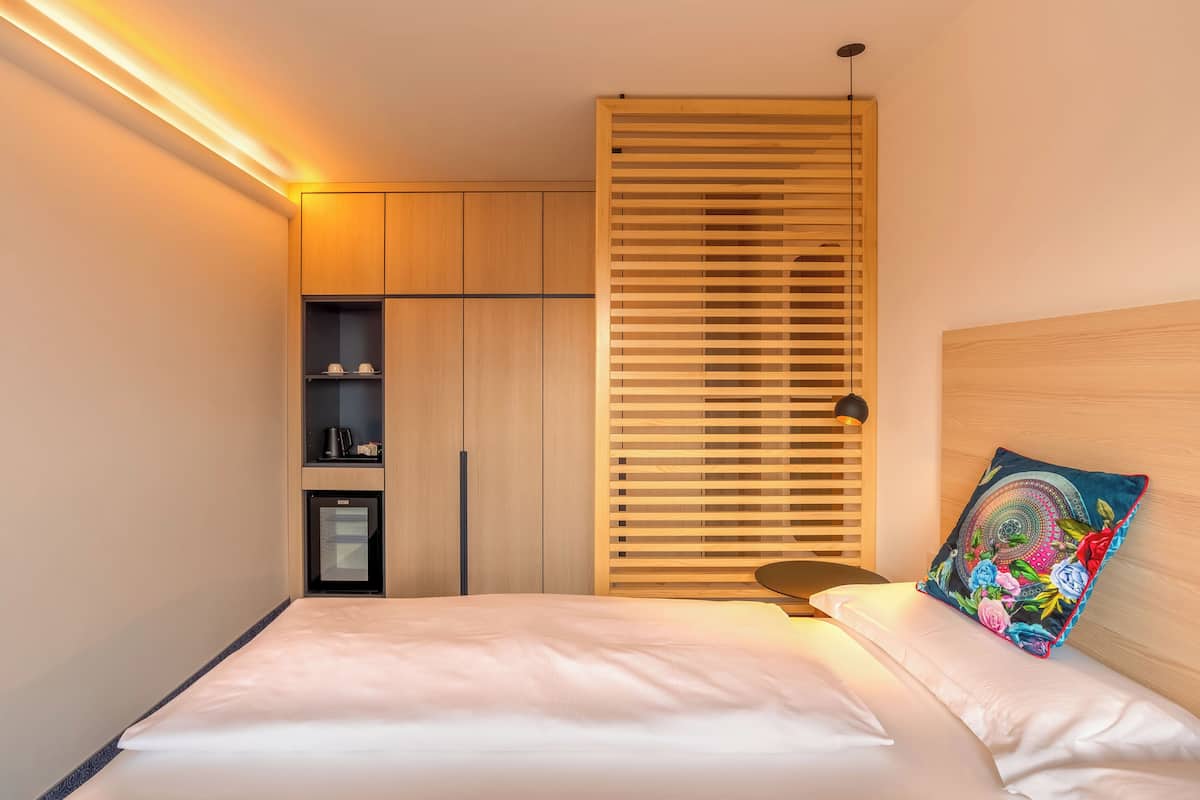 A modern bedroom with a bed, a wooden wardrobe, a built-in shelf, and a decorative pillow.