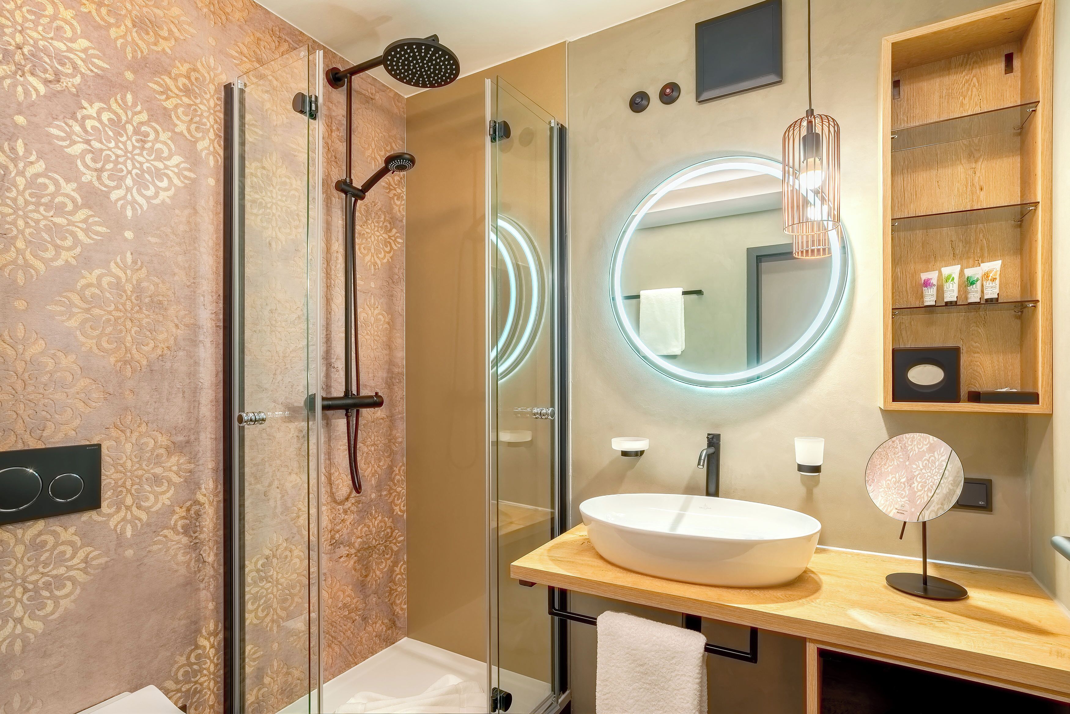 Een moderne badkamer met een douchecabine van glas, een ronde spiegel met verlichting, en een houten wastafelmeubel met een ruime wasbak.