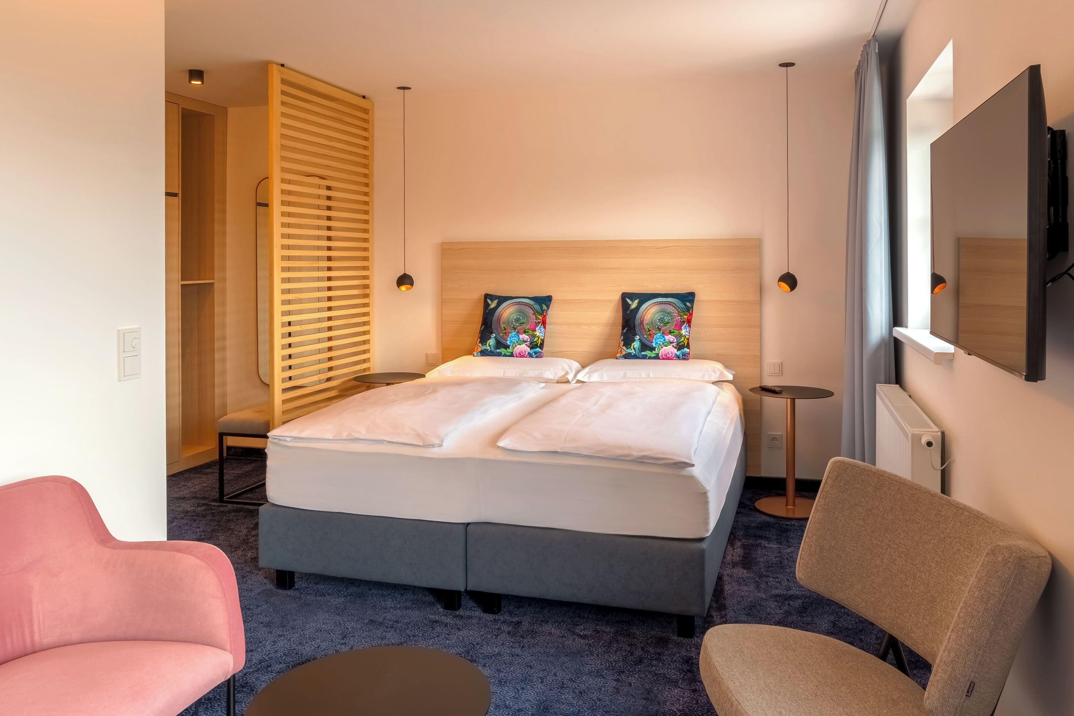 Una habitación de hotel con una cama, dos sillas, una mesita, un espejo y un armario.