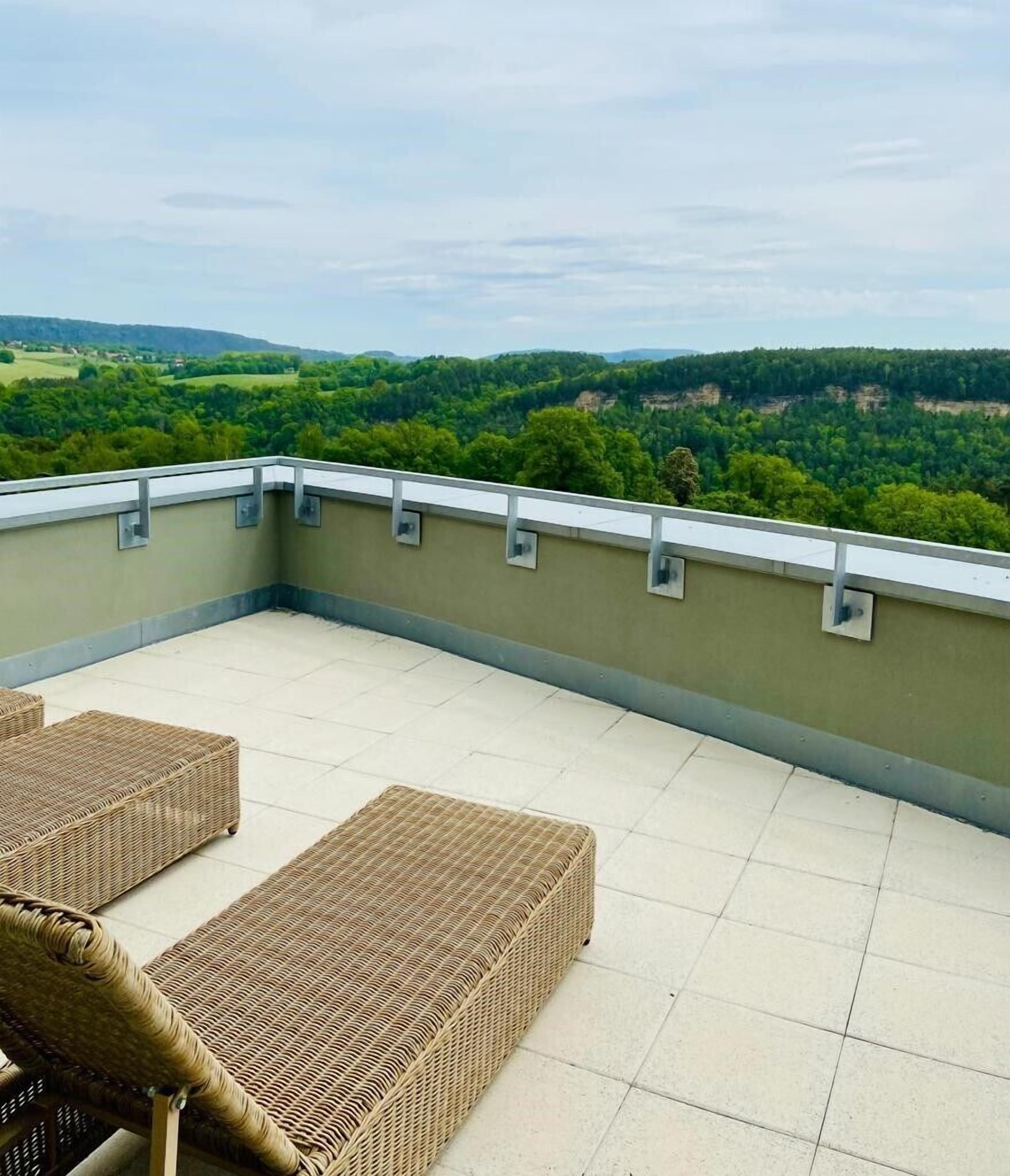 Eine Dachterrasse mit zwei Korbstühlen und Blick auf eine grüne Landschaft.