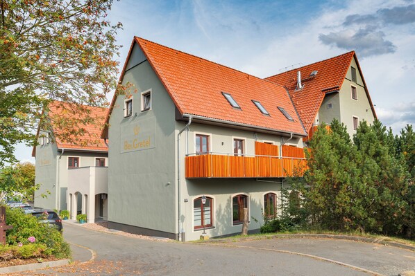 A two-story building with a red-tiled roof, a balcony with orange awnings, and a sign that reads "Bei Gretel."