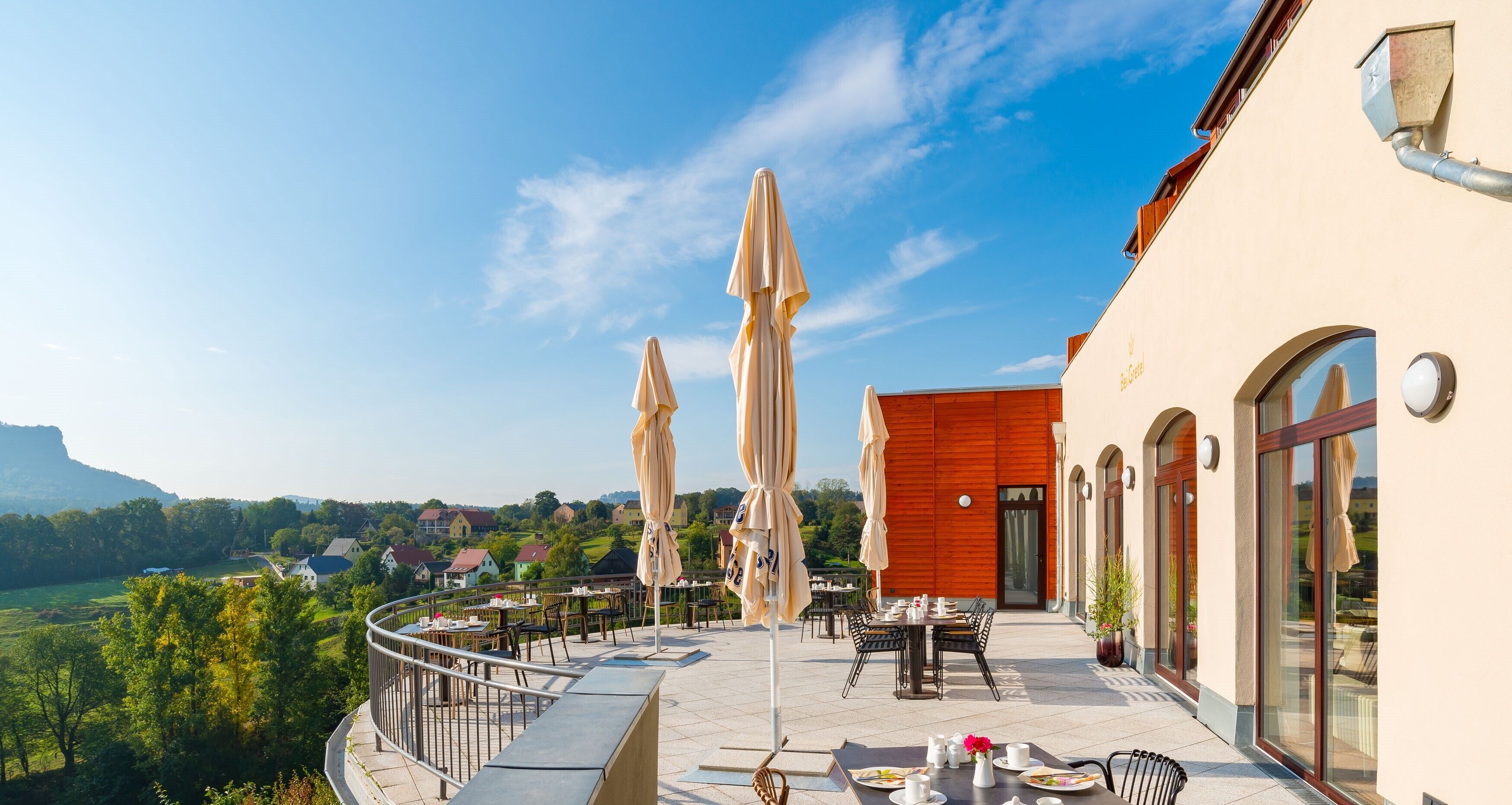 An outdoor terrace with tables and chairs, umbrellas, and a view of the countryside.
