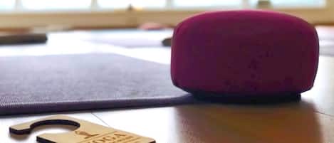 Una colchoneta de yoga, un cojín rosa y un bloque de yoga sobre un piso de madera.