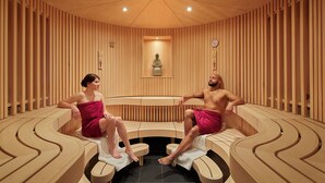 Eine Sauna mit hölzernen Bänken, die halbkreisförmig angeordnet sind, einer zentralen Statue und einer an der Wand befestigten Uhr.