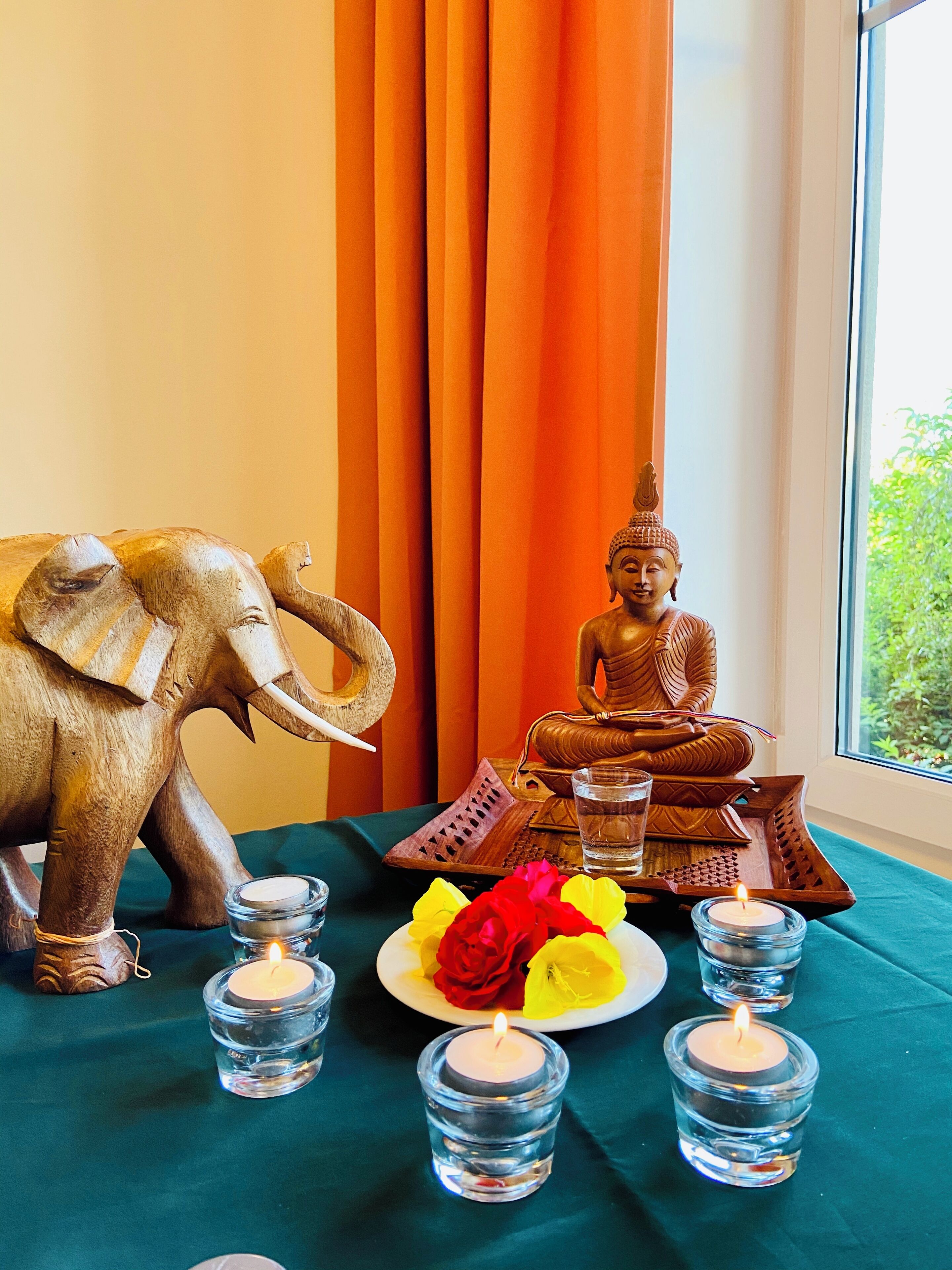 Ett rum med en Buddha-staty, en elefantstaty och ett bord med ljus och blommor.
