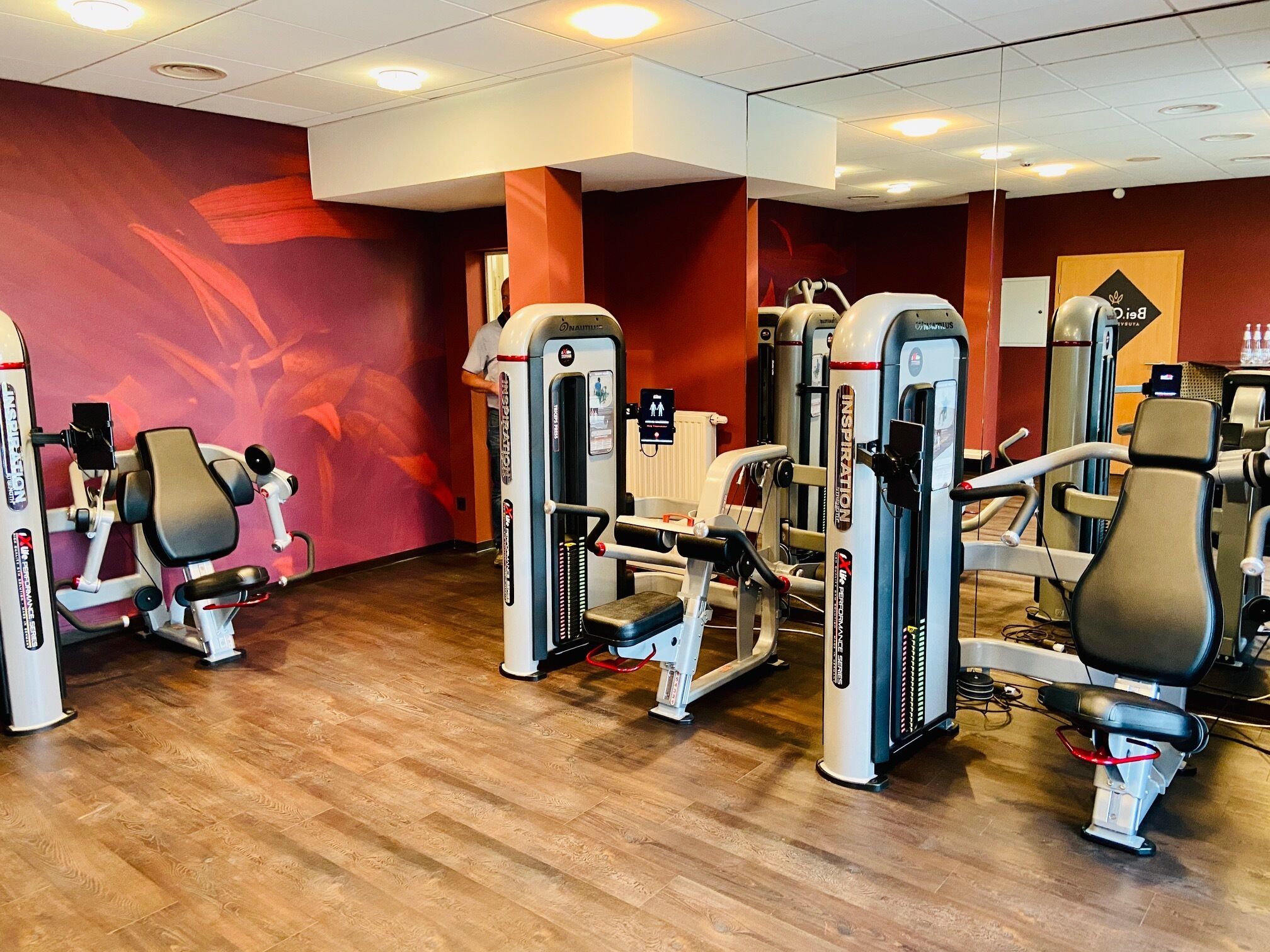 Ein Fitnessstudio mit verschiedenen Trainingsgeräten, Holzboden und roten Wänden.