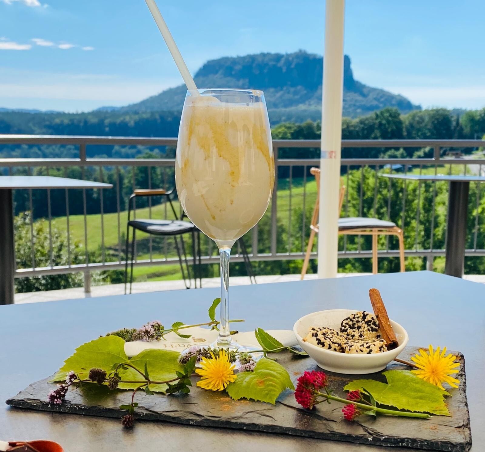Un vaso de bebida blanca sobre una mesa, con una vista panorámica de montañas al fondo.