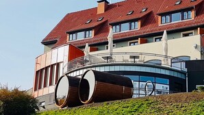 Ein modernes Gebäude mit rotem Ziegeldach, großen zylindrischen Elementen und einem Balkon mit Geländern.