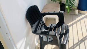 A corner of a room with a black plastic chair, a small table, and a potted plant.