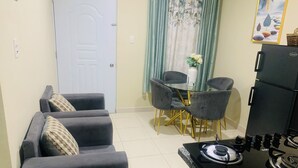 A compact kitchen with a gas stove, a dining table with chairs, and a sofa with cushions.