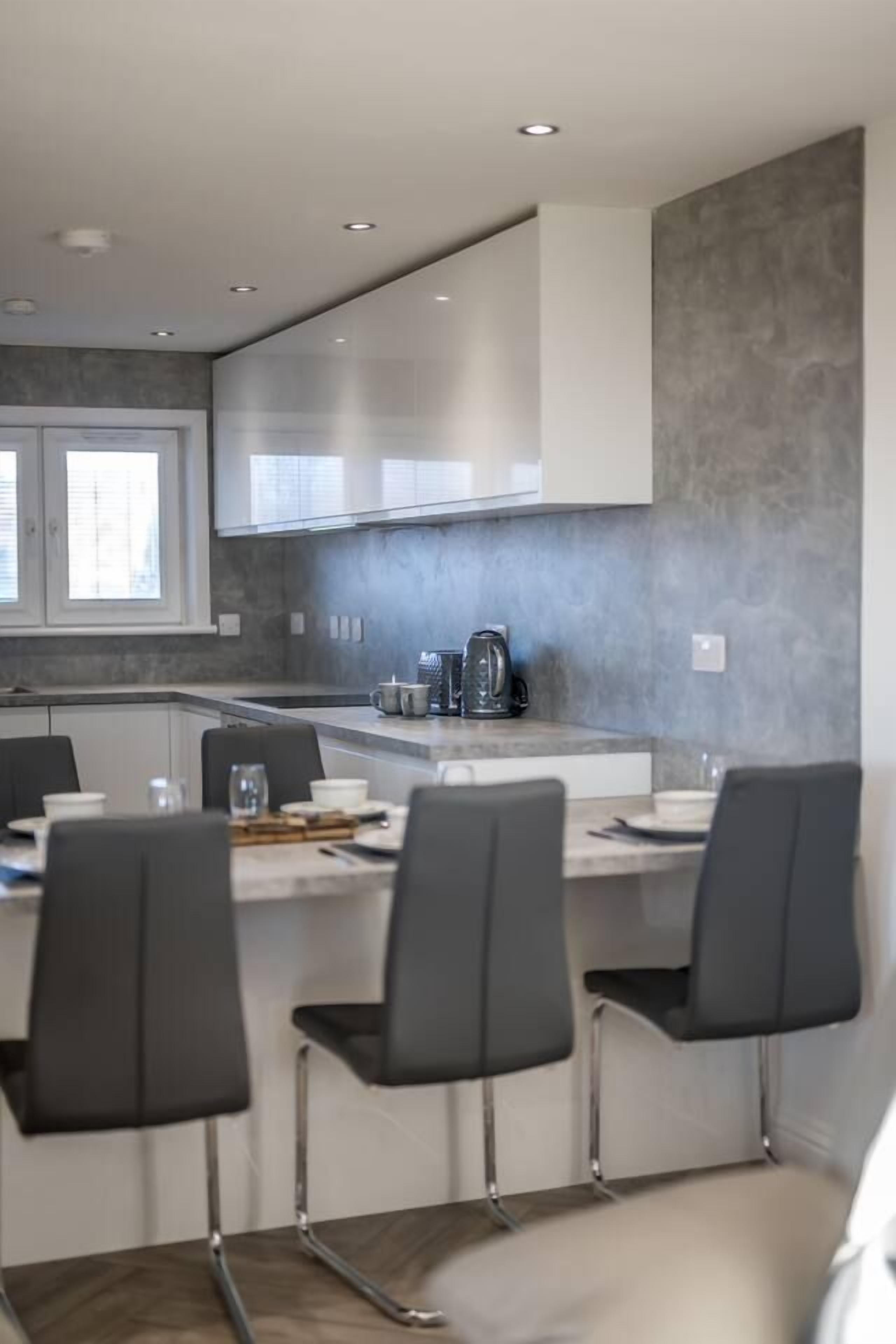 A modern kitchen with a central island, bar stools, and a coffee machine.