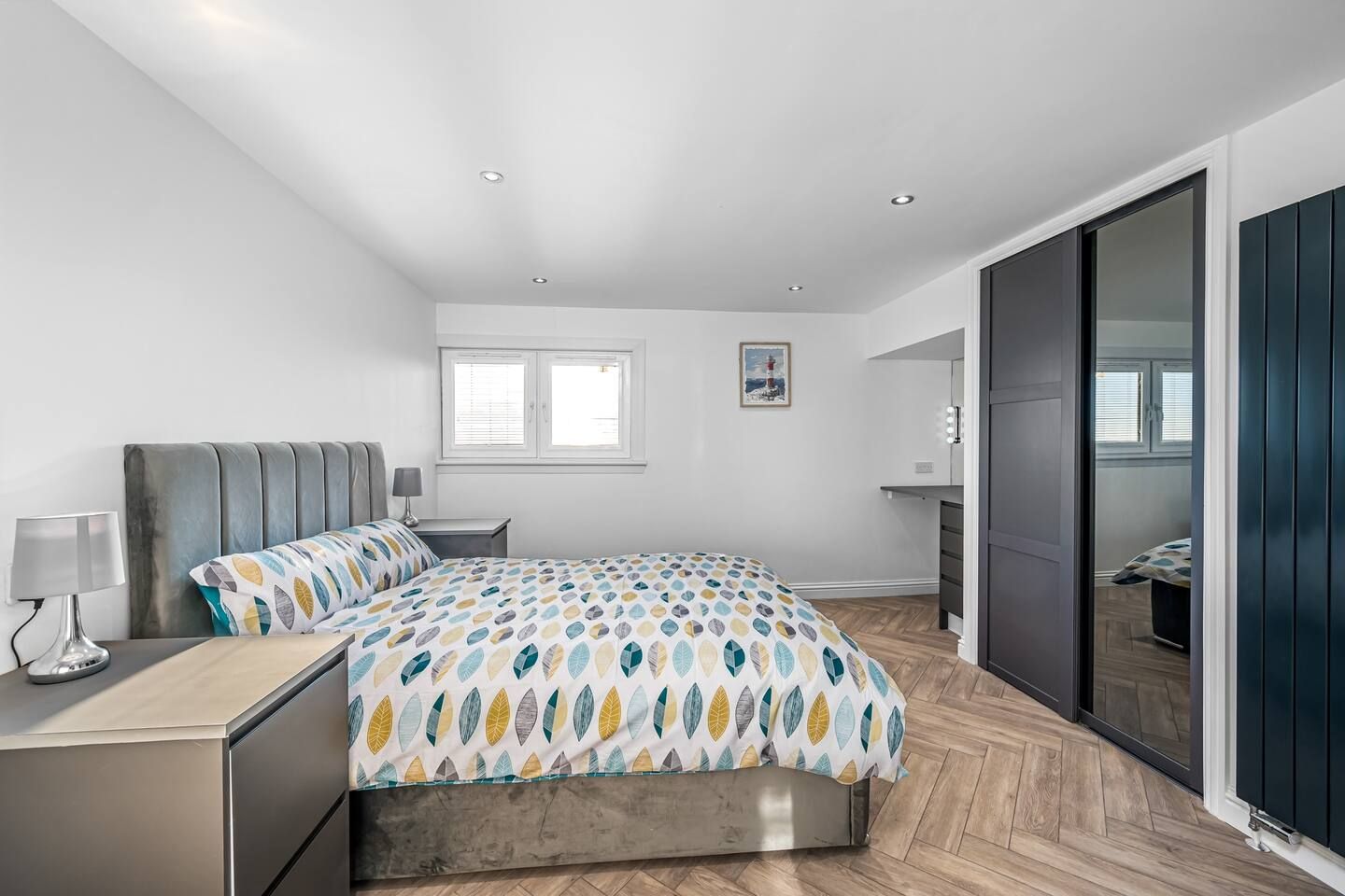 A modern bedroom with a bed, bedside table, lamp, and a large window.