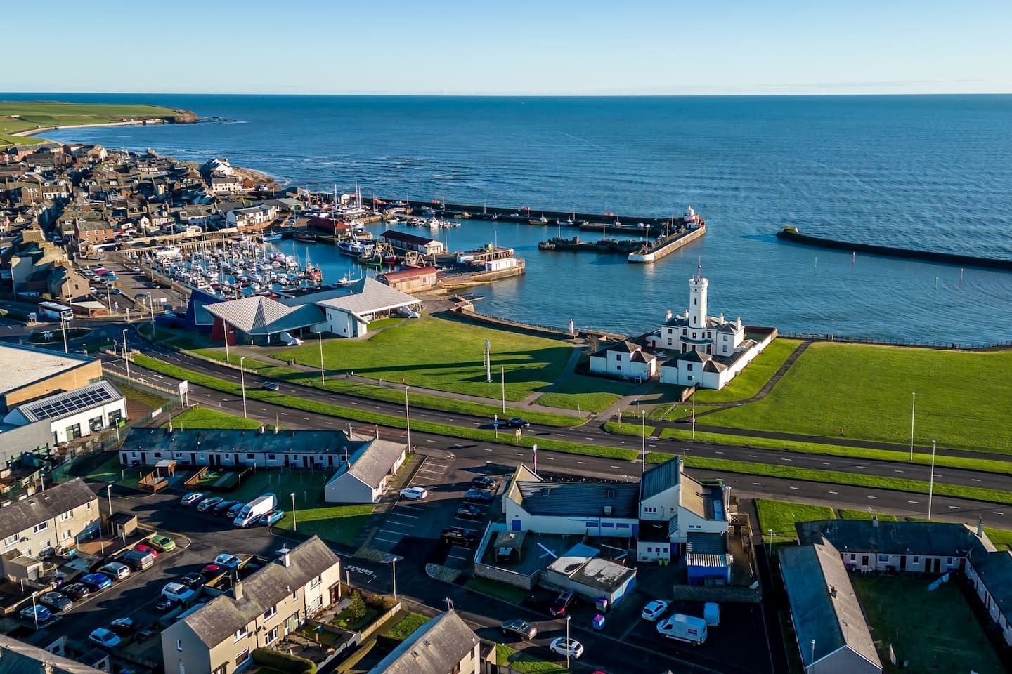 An aerial view of a coastal town with a marina, a lighthouse, and a mix of residential and commercial buildings.
