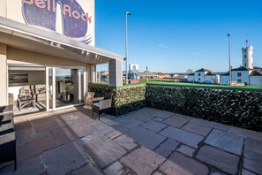 Un hôtel doté d’un patio, d’une enseigne indiquant la présence d’un restaurant, et offrant une vue sur la mer et les bâtiments situés au loin.