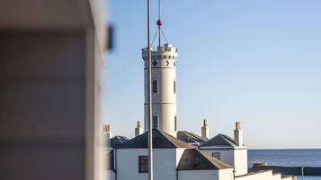 Un phare à l’extérieur blanc et doté d’une haute tour, situé dans une zone herbeuse offrant une vue dégagée sur la mer.