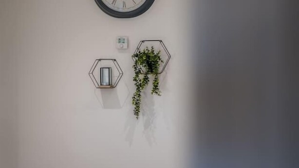 A room with a wall-mounted clock, a hexagonal light fixture, and a hanging plant. - Sea Views Luxury Apartment Free Parking - Coast Ap (Arbroath)