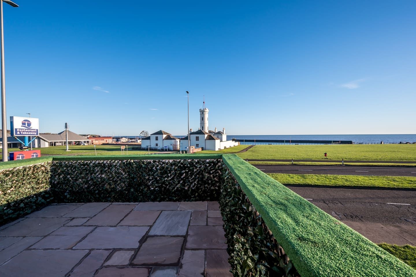 A coastal view with a restaurant sign, a white building with a tower, and a clear sky.