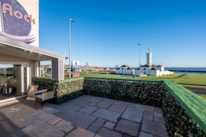A coastal hotel with a patio area, a view of the sea, and a lighthouse in the distance. - Sea Views Luxury Apartment Free Parking - Coast Ap (Arbroath)