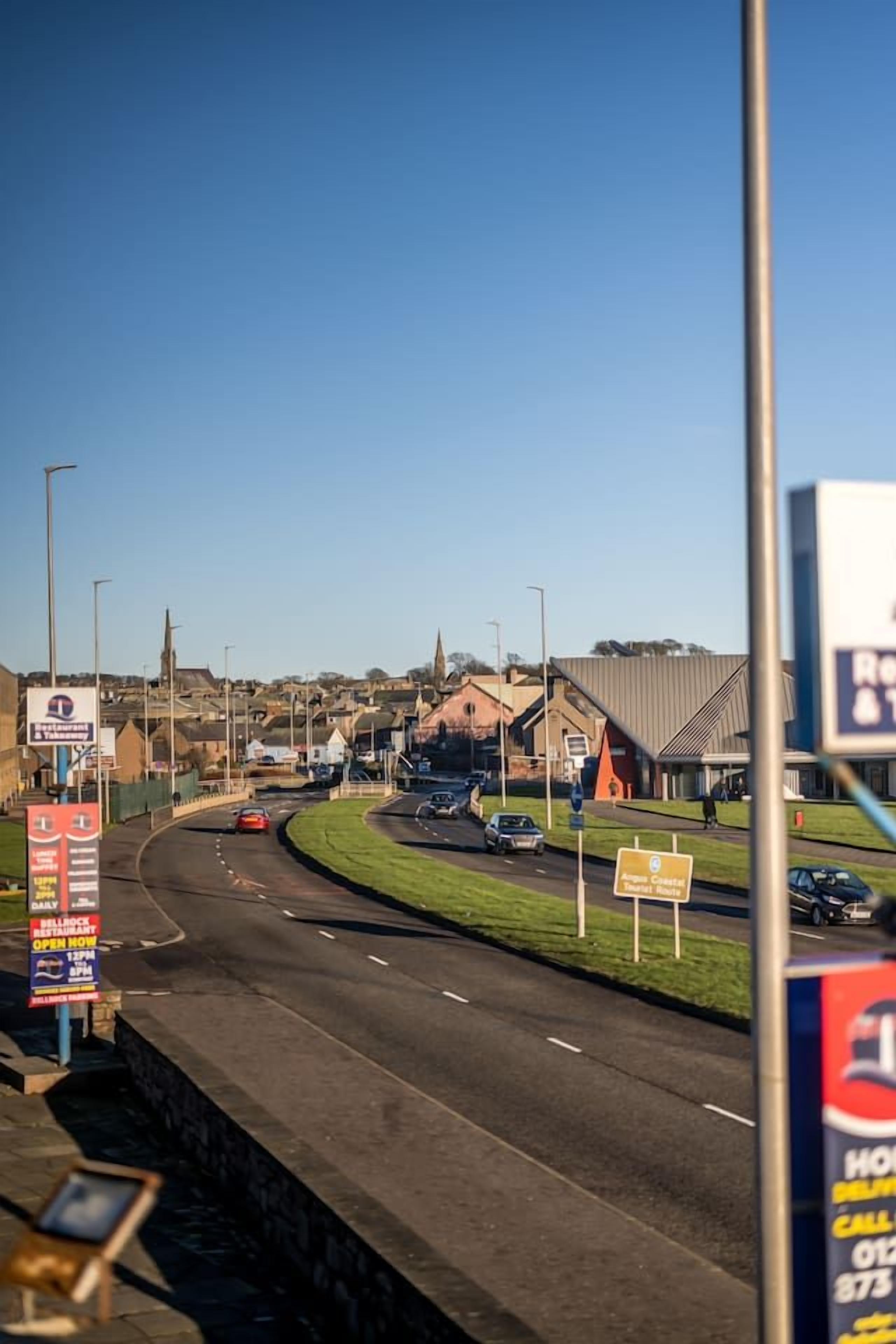 A road with multiple lanes and a roundabout. There are signs for a restaurant and a hotel.