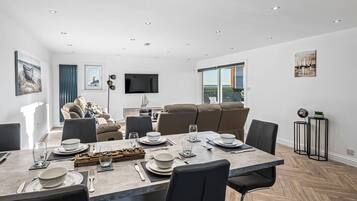 A modern dining area with a large table set for four, a sofa, and a television mounted on the wall.