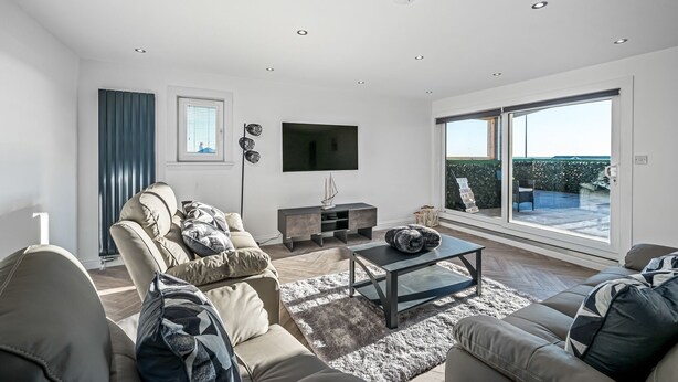 A modern living room with a sofa set, a coffee table, and a TV mounted on the wall. - Luxury Apartment with Sea Views Balcony (Arbroath)