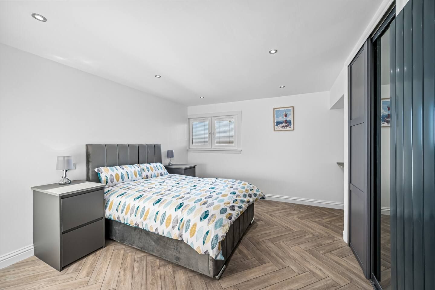 Een moderne slaapkamer met een bed, nachtkastjes, een raam en een deur.