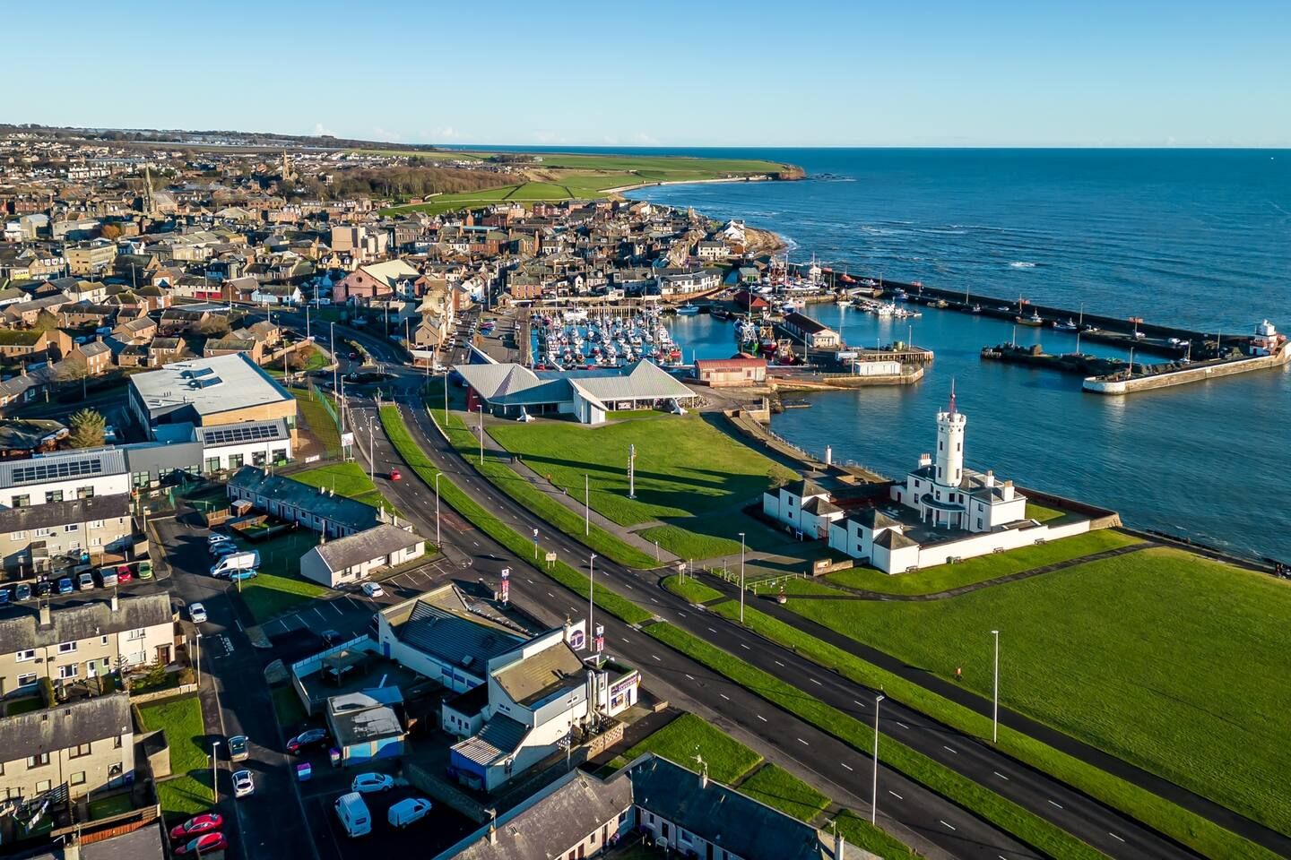 An aerial view of a coastal town with a prominent lighthouse, a marina, and a mix of residential and commercial buildings.