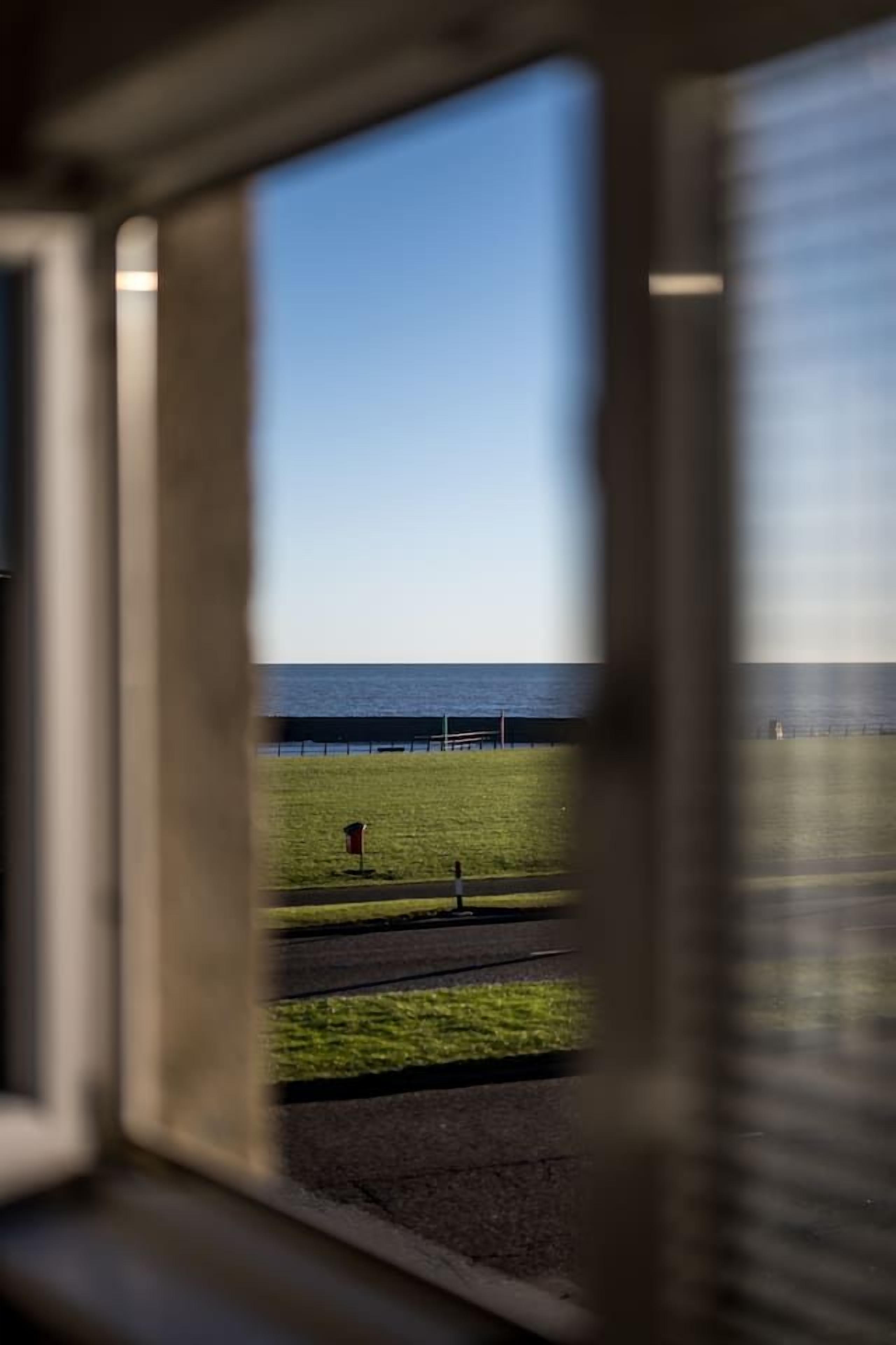 A view through a window with a grassy area, a fence, and a body of water.
