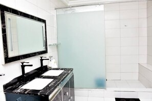 Kylpyhuoneessa on kaksi pesuallasta, suuri peili ja suihkutila.