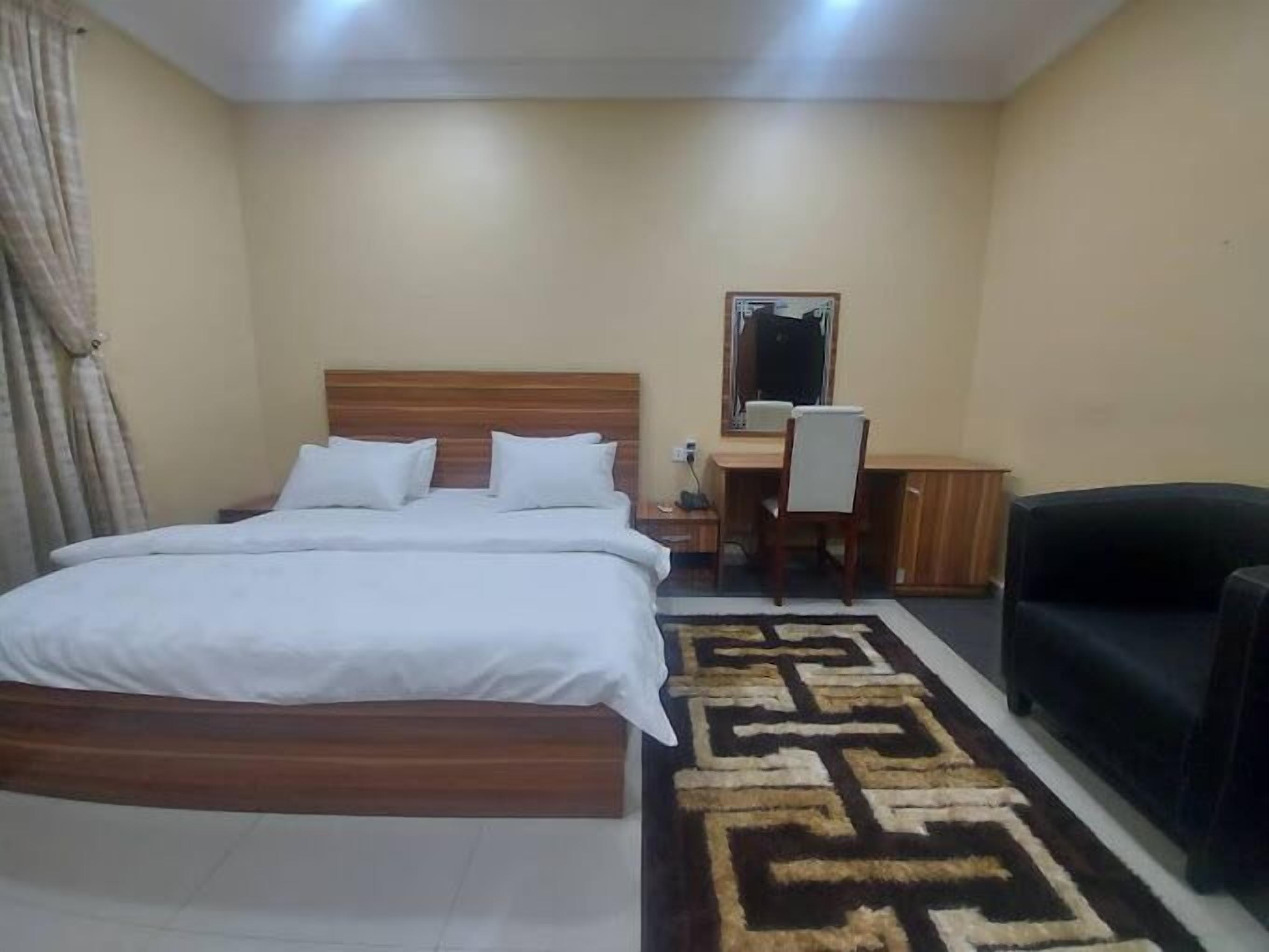A bedroom with a bed, a desk, a chair, and a sofa.