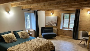 Een gezellige slaapkamer met een groot bed, een stoel, een bureau en een raam met gordijnen.