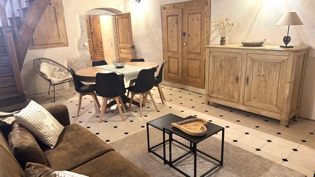 Een gezellige woonkamer met een bruine bank, een eettafel met stoelen, een houten kast en een lamp.