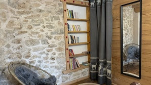Een gezellige kamer met een stenen muur, een houten boekenkast, een rieten stoel, een spiegel en een kamerbreed tapijt met patroon.