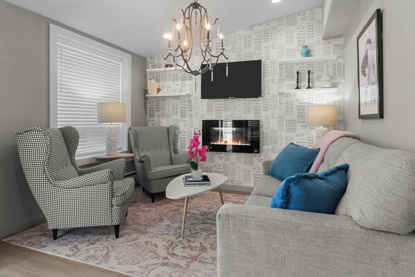 A living room with a fireplace, checkered armchairs, a sofa, and a chandelier.
