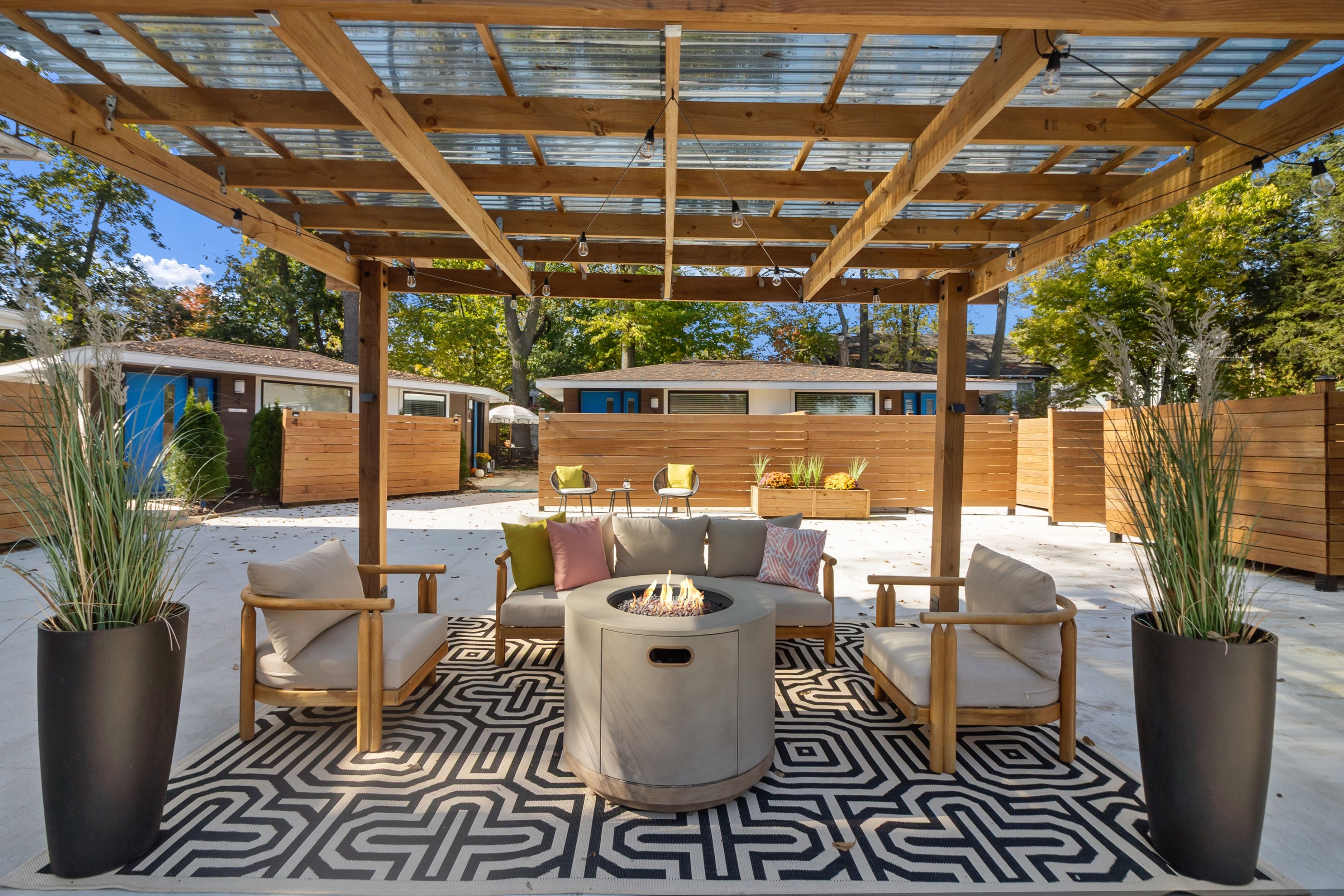 A covered outdoor seating area with a fire pit, wooden furniture, and a patterned floor.