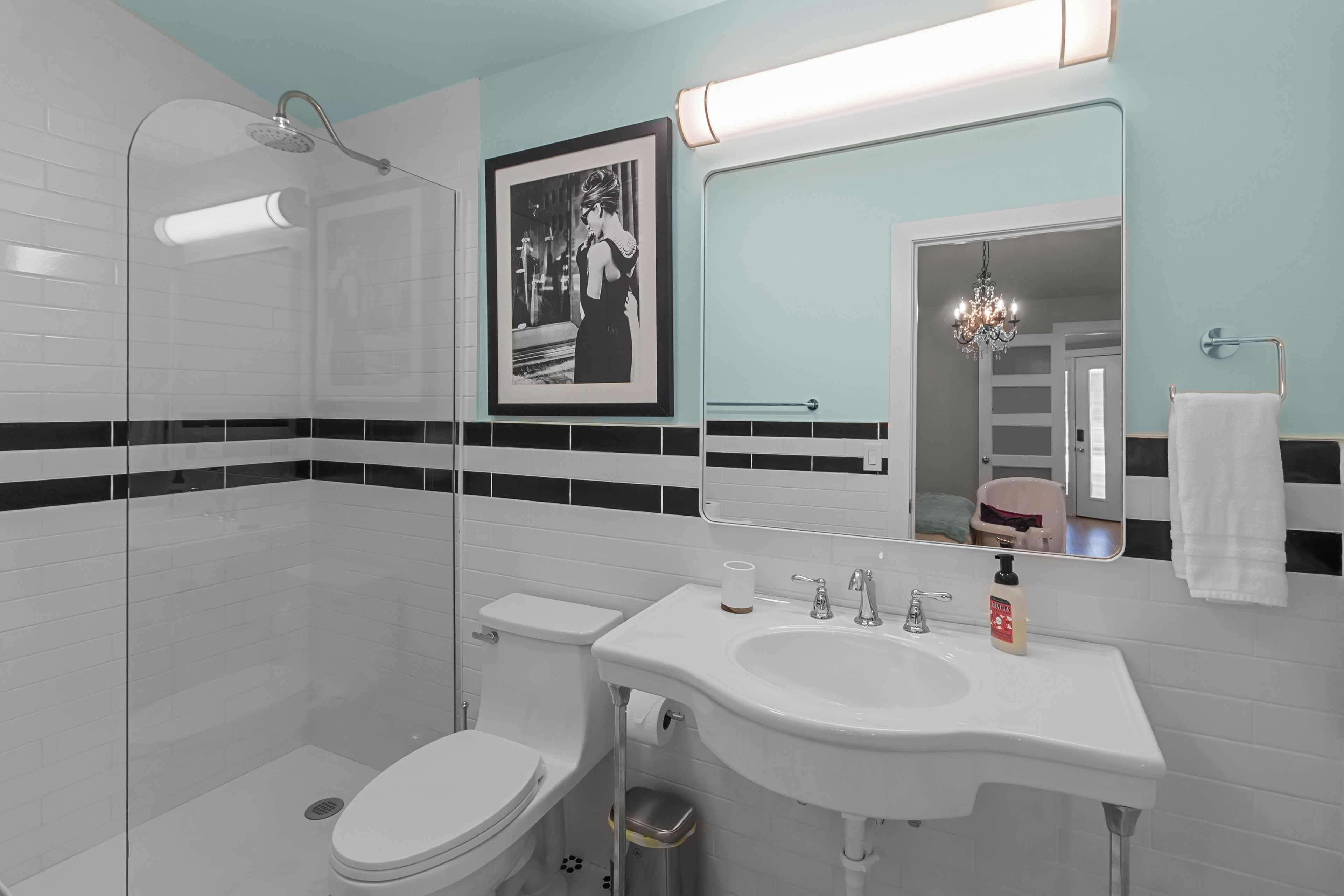 Une salle de bain moderne avec une douche à parois de verre, un lavabo blanc et un tableau encadré au mur.