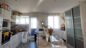 A modern kitchen with white cabinets, a dining table with a beige tablecloth, and a large window. - Beautiful, quiet, bright artist's apartment.  South-facing terrace, air conditioning. (Marseille)