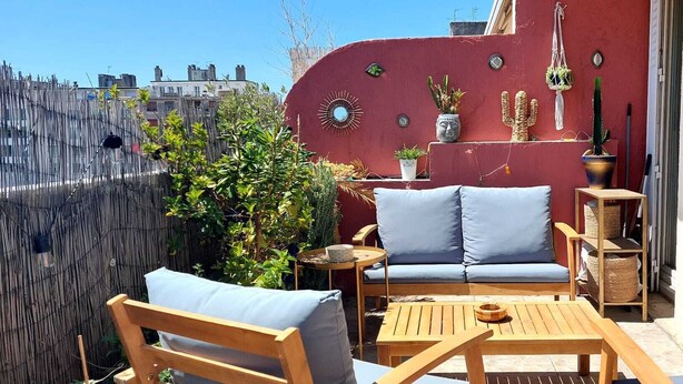 A cozy outdoor seating area with a red wall, a blue sofa, wooden chairs, and a small table. - Beautiful, quiet, bright artist's apartment.  South-facing terrace, air conditioning. (Marseille)