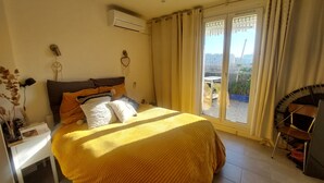 A bedroom with a large bed, an air conditioning unit, a bedside table, a chair, and a view of the outdoors. - Beautiful, quiet, bright artist's apartment.  South-facing terrace, air conditioning. (Marseille)