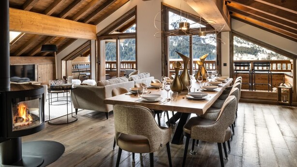 A spacious dining area with a long table set for six, a fireplace, and a view of the mountains through large windows.