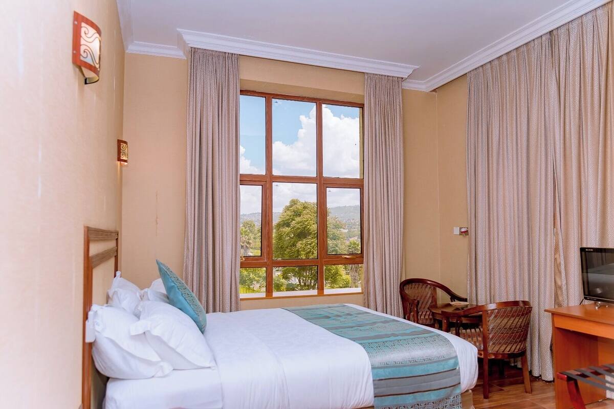 A hotel room with a large bed, a desk with a chair, a television, and a window with curtains.