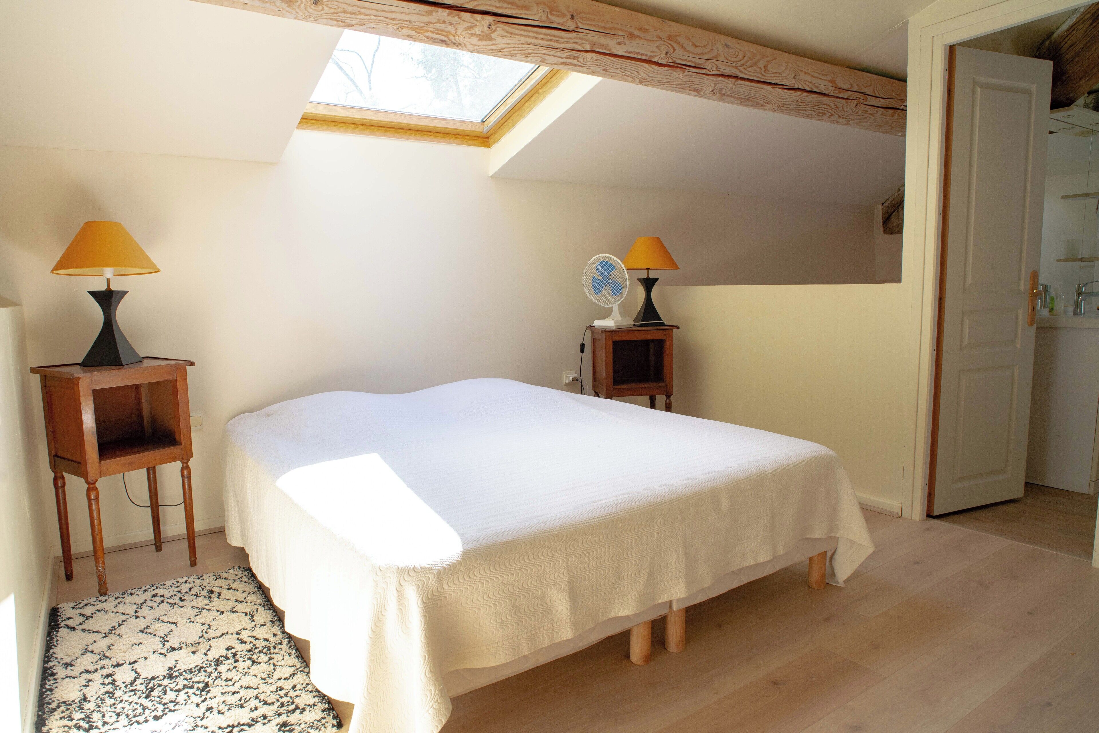 Une chambre avec un puits de lumière, un lit, deux tables de chevet avec des lampes et un petit miroir.