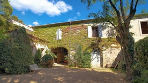 A courtyard with a gravel path, a bench, and a building partially covered with ivy. - Harvesters' house (Aigues-Vives)