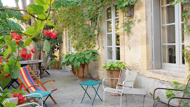 An outdoor patio with various seating options, including chairs and tables, surrounded by greenery and potted plants. - Harvesters' house (Aigues-Vives)