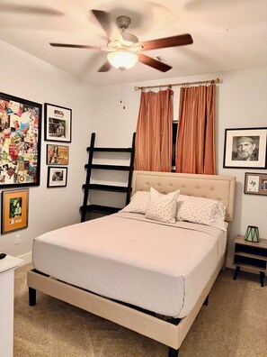 A bedroom with a bed, a ceiling fan, a window with curtains, and various framed pictures on the wall. - Bertram Tranquility- 3 Bedroom 2 Bath Hideaway (Bertram)